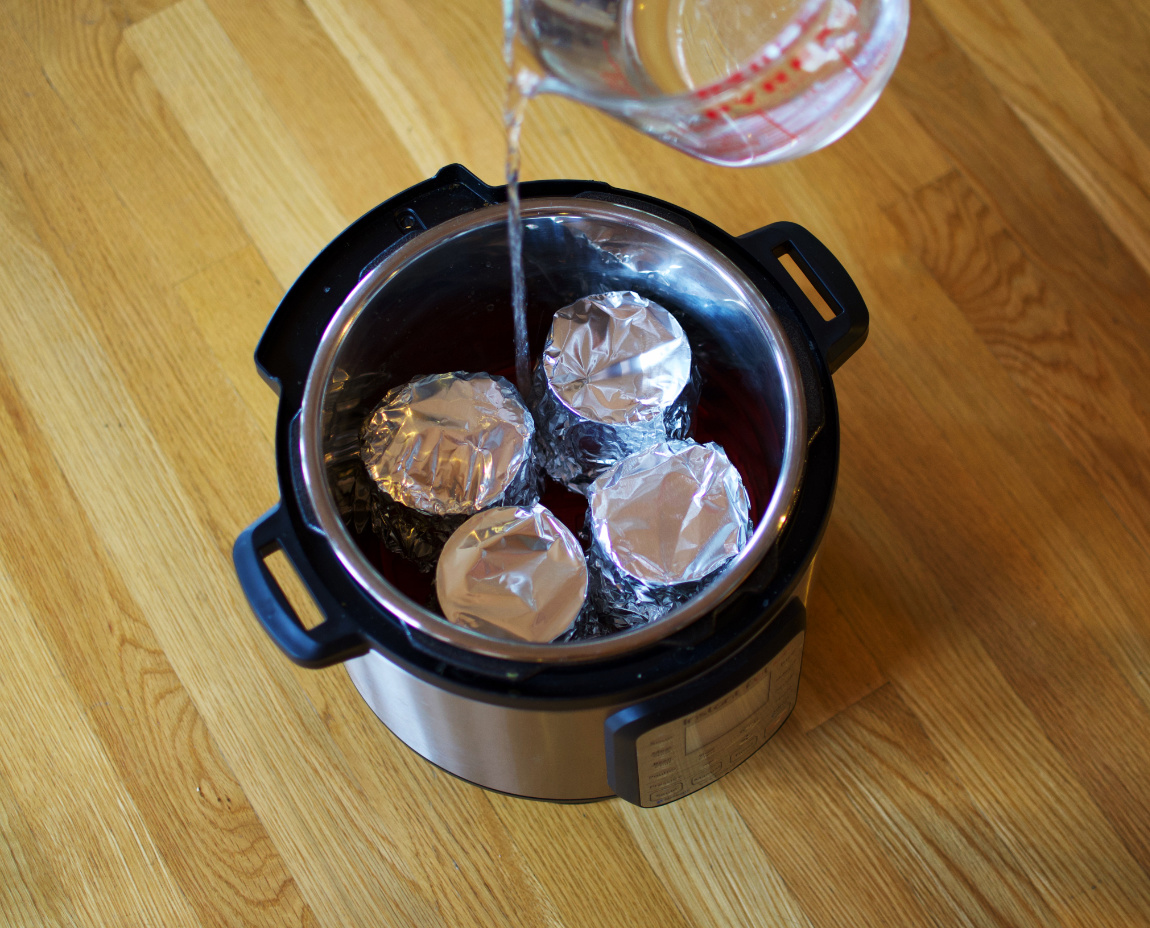 Four cans of condensed milk in an Instant Pot with water being added.