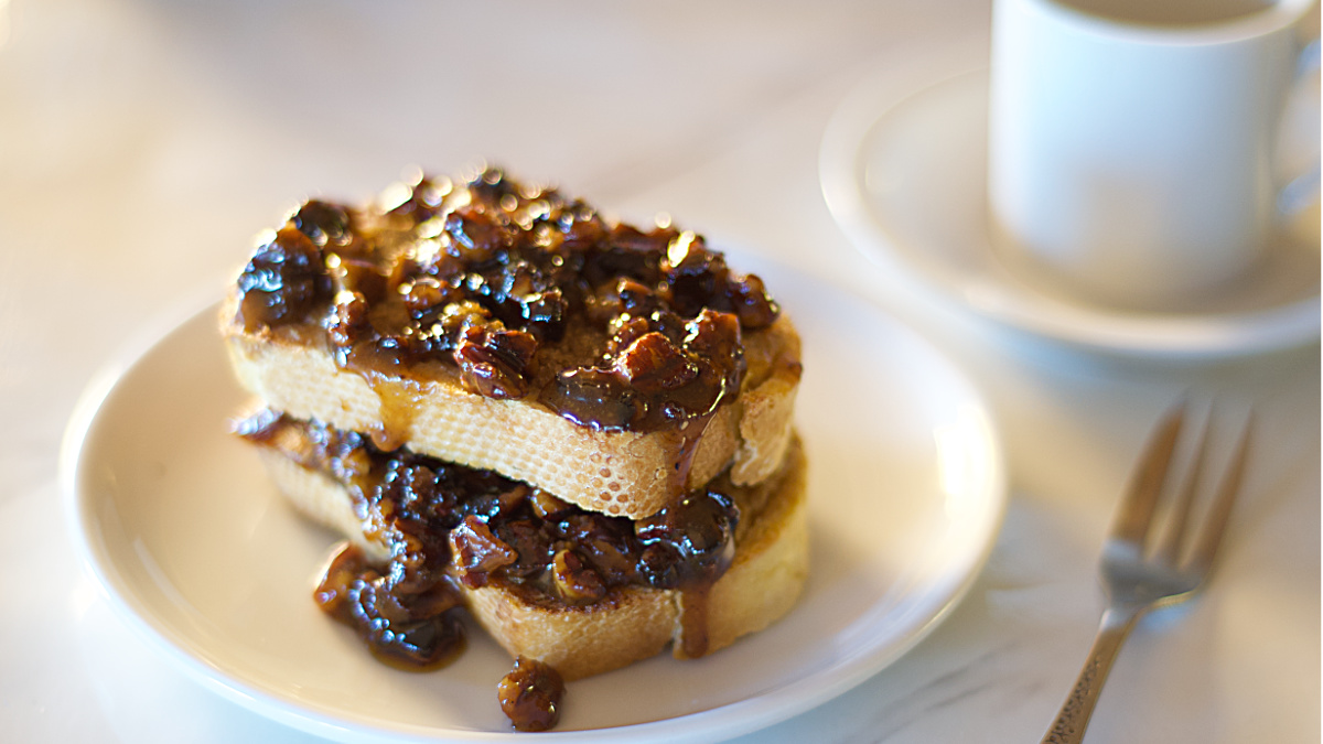 Pecan Pie French Toast served on a plate with a small fork and coffee cup in the background.