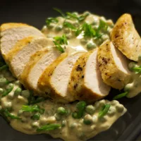 Sliced of cooked chicken breast served with a creamy sauce with peas.
