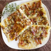 Three pieces of Flammkuchen on a plate garnished with thyme.