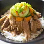 Chinese Shredded Pork served in a black bowl with rice and Asian vegetable salad as a garnish.