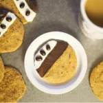 Decorated Espresso Cookie on a plate with other Cookies surrounding it, served with a cup of tea.