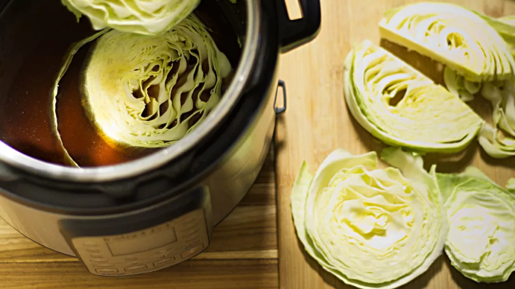 Slices of raw green cabbage being placed into the slow cooker with water and other ingredients in it.