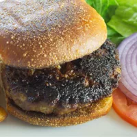 Black and blue burger served on a bun with lettuce, tomato, and onion on the side.