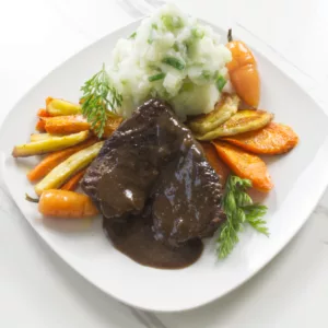 plate of braised pot roast with carrots, parsnips, and champ served on a white plate.