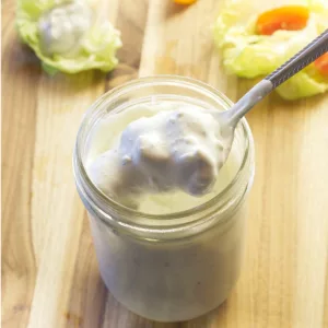 Spoonful of Chunk Blue Cheese Dressing being removed from a mason jar of it. Peppers and lettuce are in the background.