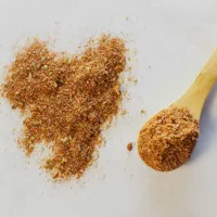 Chorizo Seasoning on a sheet of white paper with a small wooden spoon beside it, The spoon contains seasoning.