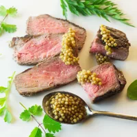 Pickled Mustard Seeds served on top of sliced steak, garnished with green herbs.