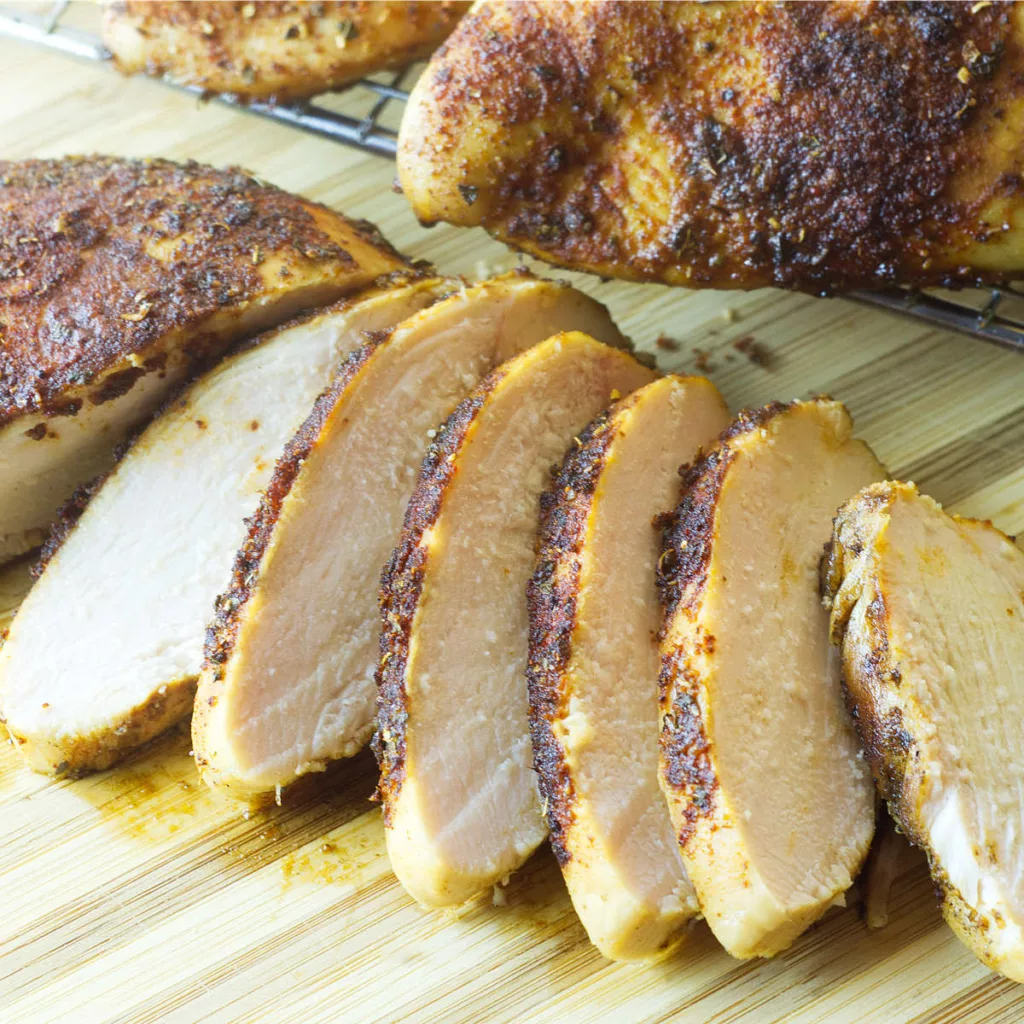 Sliced Smoked Chicken Breast on a board with whole chicken breast in the background
