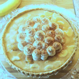 Banoffee pie on a glass plate with a banana and serving slicer in the background.
