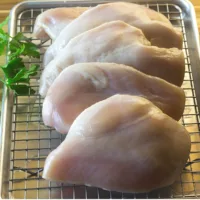 Chicken breasts brined and ready to be cooked with a parsley garnish.