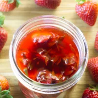 Strawberry top vinegar in a mason jar with strawberries scattered around the jar,
