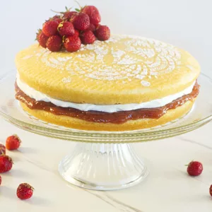 Strawberry Sponge cake on a cake pedestal with strawberries decorating it and strawberries surrounding it.