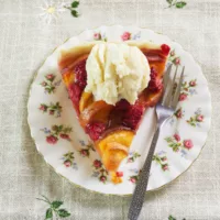 Peach Melba Tart on a plate topped with vanilla ice cream, with a fork on the side.