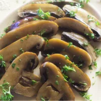Sliced simple air fried Portobello Mushrooms on a white platter, garnished with parsley pieces.