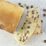 Loaf of Ice Cream bread with 2 slices cut on a marble board and surrounding raisins.