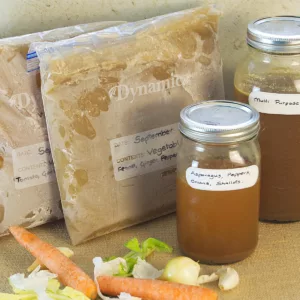 Different types of Vegetable Stock, 2 types are frozen in freezer bags, 3 types in mason jars, some vegetables in the foreground.
