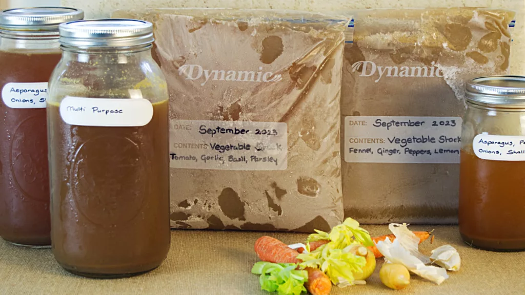 Different types of Vegetable Stock, 2 types are frozen in freezer bags, 3 types in mason jars, some vegetables in the foreground.