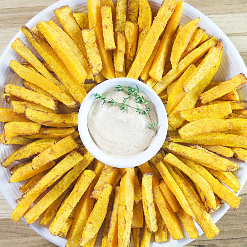 Plate of Crispy Butternut Squash Fries Air Fryer fanned out with a dish of dipping sauce in the middle garnished with fresh thyme.
