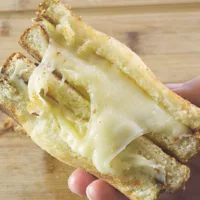 Hand held Brioche Grill Cheese Sandwich split in two showing melted cheese.