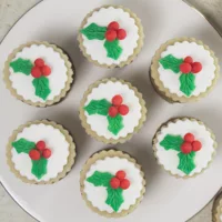 7 Mini Christmas Cakes on a white plate, each cake is decorated with marzipan, fondant and marzipan berries and leaves.