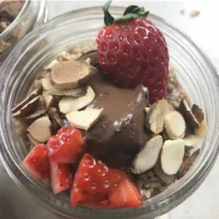 Single glass jar of Nutella Overnight Oats garnished with fresh strawberries, and toasted almonds.