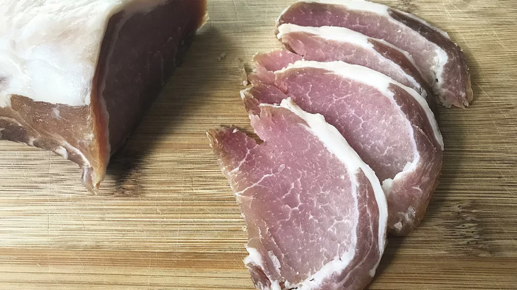 4 slices of raw Irish Back Bacon sliced on a wooden board with the whole bacon in the background.