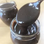 Jar of Microwave Hot Fudge Sauce with a spoon full of sauce dripping down into he jar.