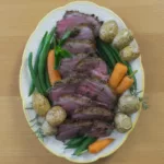 Platter containing sliced roasted Lamb Sirloin, carrots, potatoes and green beans.