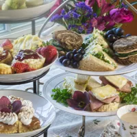 Two tiered stands filled with scones, sandwiches and pastries. Flowers in the background.