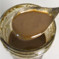 Glass jar containing Balsamic Basil Vinaigrette. A spoon is holding some of the dressing for a close up view.