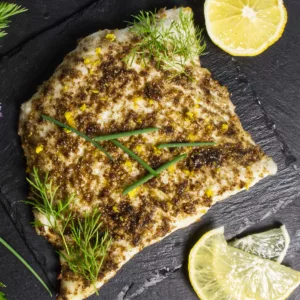 Air Fryer Halibut on a black platter, lemon slices surround it.