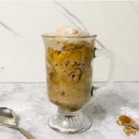 5 Minute Carrot Cake in a Mug topped with frosting with a spoon to the left and another spoon containing cinnamon to the right.