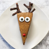 Slice of Chocolate Mousse Cake on a white plate showing chocolate antlers, eyes and a red nose.