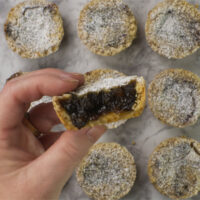 Nine Mince Pies with Crumble Topping on a marble board. One has been split revealing the pie filling.