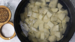 Pot filled with water and uniform pieces of potatoes. To the side is a salt container.