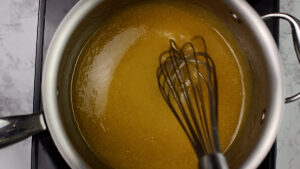 Melted sugar and golden syrup in a pot with a whisk.