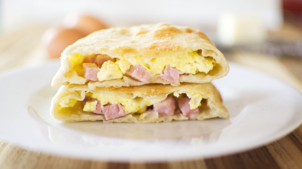 One Ham and Cheese Hot Pocket cut in two with one half sitting on top of the other half. Contents showing - ham, cheese and eggs.