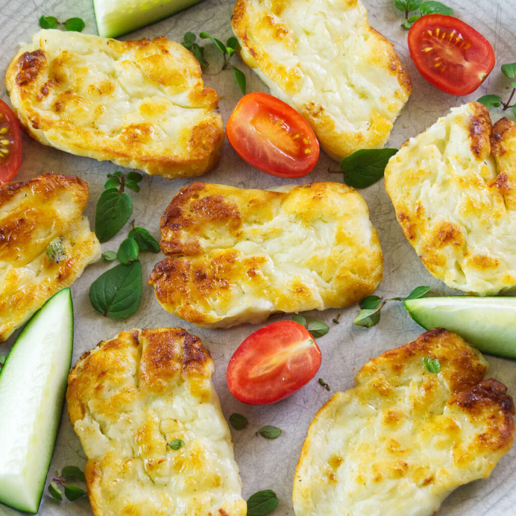 Crispy air fryer Halloumi on a plate decorated with cherry tomatoes, cucumber wedges and fresh oregano.