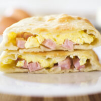 One Ham and Cheese Hot Pocket cut in two with one half sitting on top of the other half. Contents showing - ham, cheese and eggs.