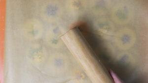 A rolling pin on top of the parchment paper under which is the pressed flower shortbread.
