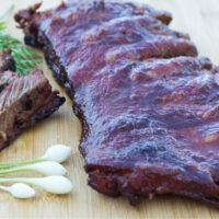 Rack of Smoked Pork Ribs on a wooden board with some sliced ribs on the side, board garnished with spring onions.