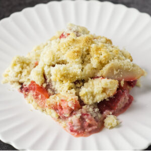 A white plate with a portion of Apple and Strawberry Crumble on it.