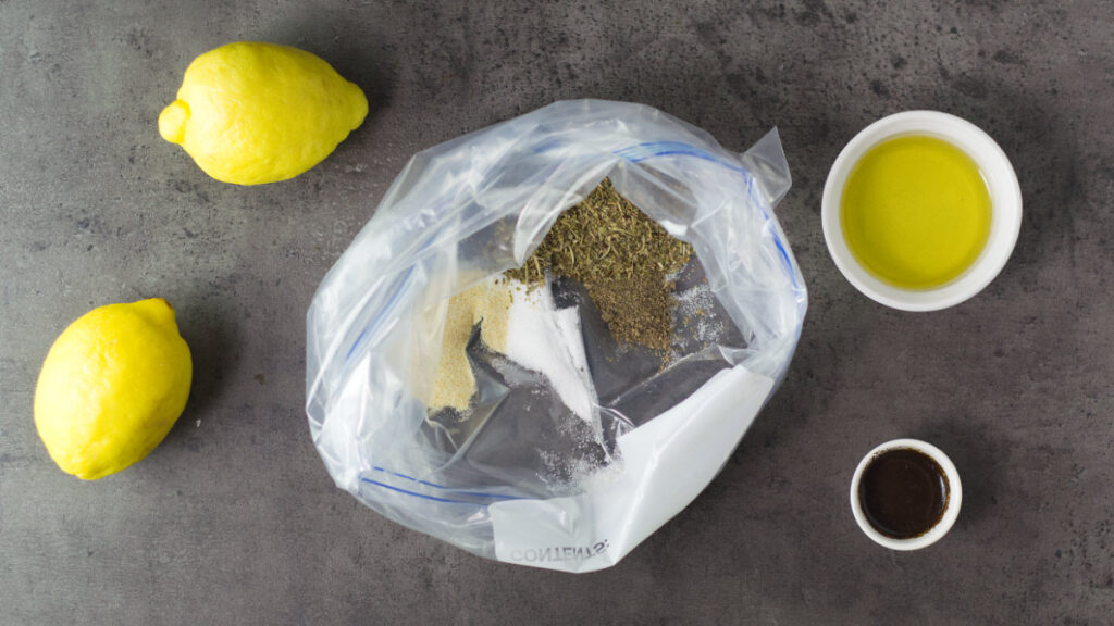 Ziplock bag containing the dry ingredients with whole lemons, olive oil and Worcestershire sauce surrounding the bag.