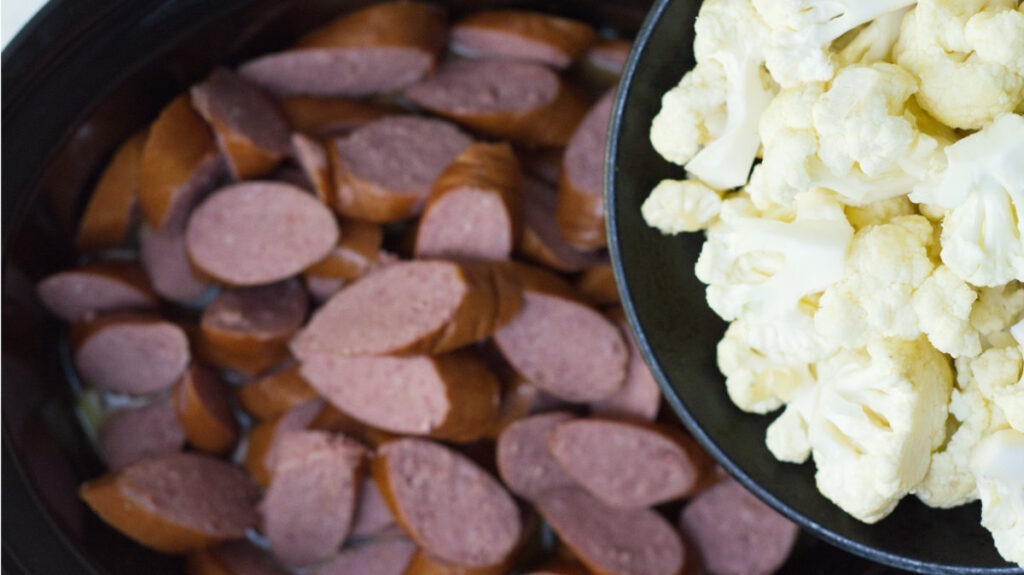 Smoked sausage slices and cauliflower are added to the  other ingredients in the black slow cooker insert.