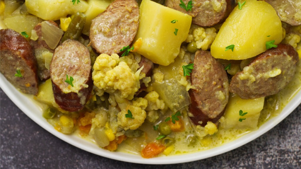 White plate containing Slow Cooker Curried Sausages garnished with little pieces of parsley.