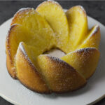 White plate with an unclose look at a completed Honeybell Cake with a dusting of powdered sugar on top.