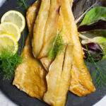 Black platter containing Smoked Trout garnished with lemon slices and fresh dill.