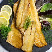 Black platter containing Smoked Trout garnished with lemon slices and fresh dill.