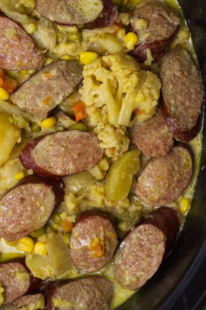 Black slow cooker insert containing Slow Cooker Curried Sausages.